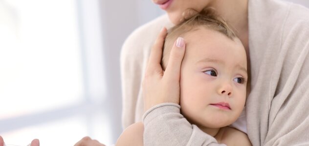 Mama tuli dziecko, któremu podawana jest szczepionka. Igła jest wbita w ramię niemowlaka. 