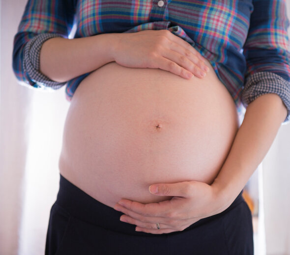 Przyszła mama stoi trzymając się czule dłońmi za brzuch. Budowanie relacji matki z dzieckiem rozpoczyna się już w czasie ciąży i ma duży wpływ na przyszłość.