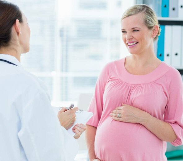 Przyszła mama jest na wizycie w gabinecie lekarskim. Kobieta uśmiecha się do lekarki, która przekazuje jej wyniki ostatnio wykonanych badań prenatalnych.