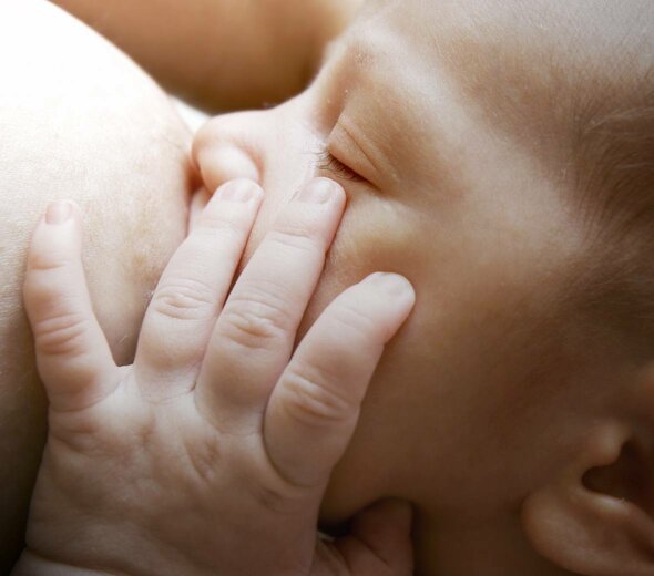 Niemowlę z zamkniętymi oczami obejmuje cały sutek matki i ssie naturalne mleko matki. Dziecko przykłada sobie rączkę do twarzy i spokojnie spożywa pożywny pokarm.