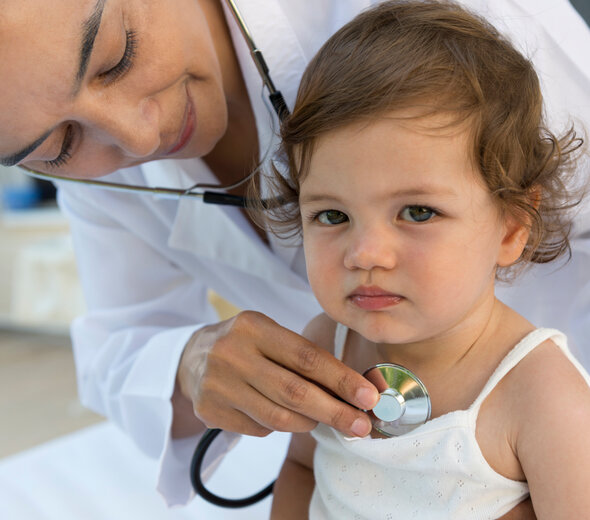 Dziewczynka z niezbyt szczęśliwa miną siedzi na fotelu w gabinecie lekarskim i klatka piersiowa jest osłuchiwana stetoskopem przez Panią doktor pediatrę.