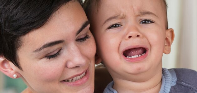 Mama stoi za synkiem i przytula go od tyłu. Dziecko ma łzy w oczach i otwartą z bólu buzię. Bóle wzrostowe u dzieci bywają bardzo przykrym doświadczeniem zarówno dla dziecka jak i rodzica.