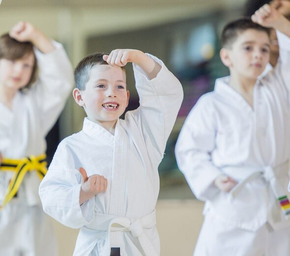 Kilkuletni chłopczyk z szerokim uśmiechem na twarzy ćwiczy karate. Rozwijanie paski, którymi interesuje się dziecko może wpłynąć na jego rozwój w późniejszym wieku.