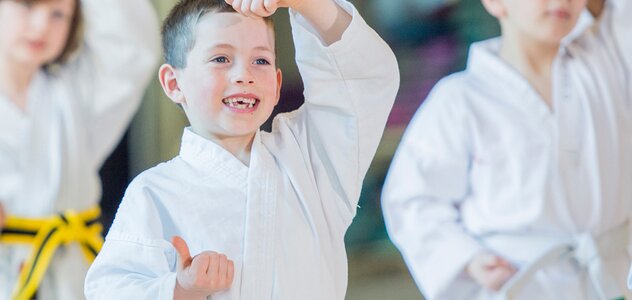 Kilkuletni chłopczyk z szerokim uśmiechem na twarzy ćwiczy karate. Rozwijanie paski, którymi interesuje się dziecko może wpłynąć na jego rozwój w późniejszym wieku.