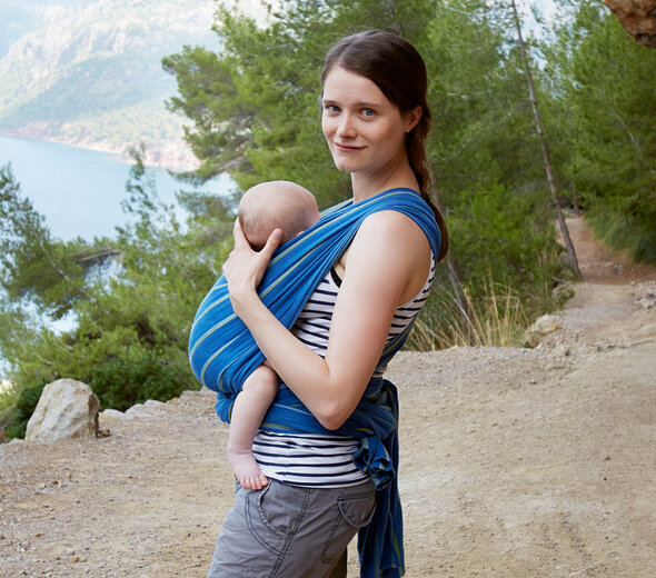 Mama z niemowlakiem na wycieczce w górach. Kobieta nosi przy sobie dziecko w starannie obwiniętej chuście do noszenia niemowlaków. Dziecko chętnie jest noszone w chuście gdyż czuje bliskość rodzica.