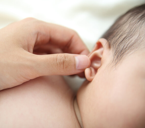 Opiekun delikatnie dotyka uszko niemowlęcia, które leży spokojnie na boczku. Dbanie o higienę dziecka jest bardzo ważne w tworzeniu się bariery ochronnej organizmu.