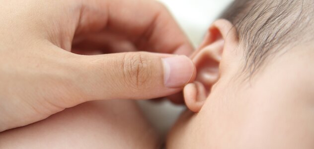 Opiekun delikatnie dotyka uszko niemowlęcia, które leży spokojnie na boczku. Dbanie o higienę dziecka jest bardzo ważne w tworzeniu się bariery ochronnej organizmu.