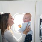 Młoda, uśmiechnięta kobieta siedzi w samolocie wraz z dzieckiem. Oboje uśmiechają się, podczas gdy matka zabawia dziecko, aby nie stresowało się nowym doświadczeniem.