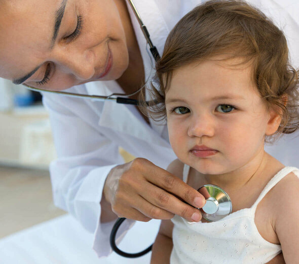 Kilkumiesięczny bobas przebywa w gabinecie lekarskim. Maluch samodzielnie, spokojnie siedzi na kozetce ubrany w podkoszulkę. Pani doktor bada płuca dziecka za pomocą stetoskopu. 