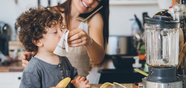 Młoda mama spędza czas razem ze swoim kilkuletnim synkiem w kuchni. Rodzina wspólnie stara się ugotować obiad. Rodzicielka wyciera chusteczką nos chłopca, a przy uchu trzyma telefon.