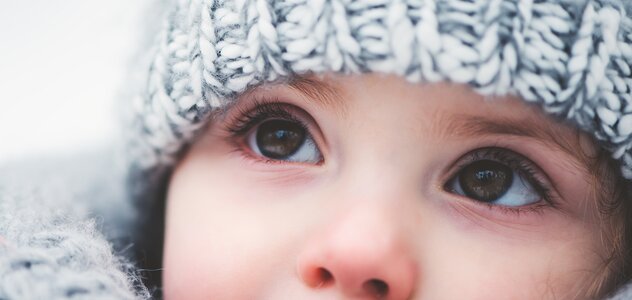 Niedawno narodzone niemowlę przebywa na świeżym powietrzu. Bobas z dużymi brązowymi oczami w zimę spędza czas w ogrodzie. Maluch owinięty jest ciepłym, grubym szalikiem i czapką.